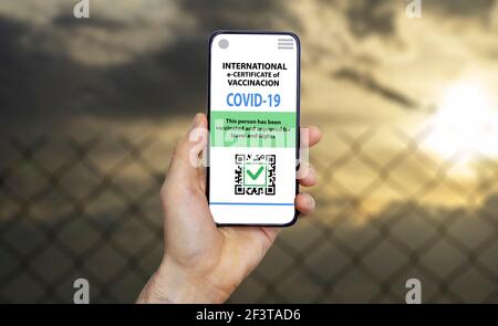 Coronavirus vaccination certificate or vaccine passport for travellers concept. COVID-19 immunity e-passport in the smartphone mobile app for international travelling. Fence against the sky. Stock Photo
