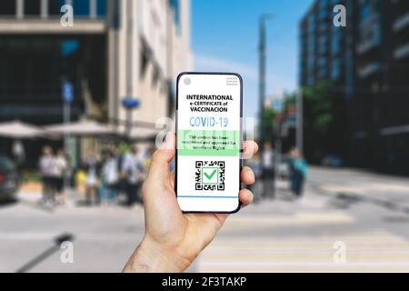 Coronavirus vaccination certificate or vaccine passport for travellers concept. COVID-19 immunity e-passport in the smartphone mobile app for international travelling. City street background Stock Photo