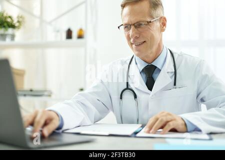Cheerful doctor using modern notebook in clinic Stock Photo