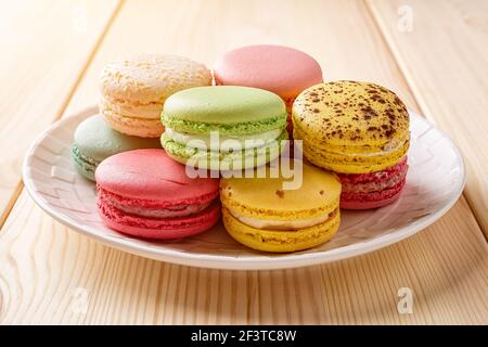 Set of multicolored macaroons on a white plate over wooden table. Colorful macaron cakes variety. Delicious french dessert. Sweets of almond flour. Stock Photo
