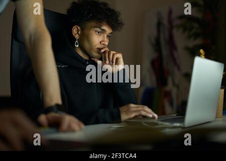 Remote work. Focused young guy with piercing sitting in front of laptop screen while working late in the evening Stock Photo