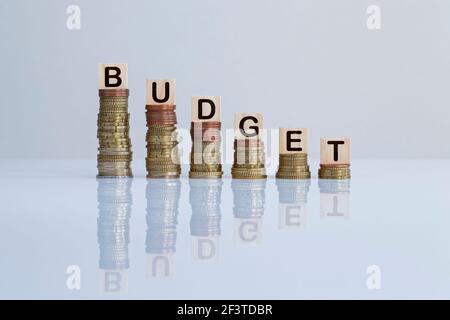 Word 'BUDGET' on wooden blocks on top of descending stacks of coins. Concept of decrease of wealth, recession, business loss and financial reduction. Stock Photo