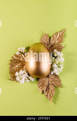 Trendy Easter background with Gold egg and golden leaves on a light green color background. Spring Festive concept Stock Photo