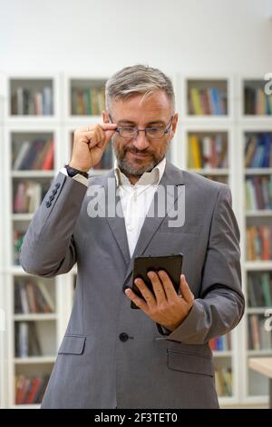 Handsome Mature Businessman or Professor Holding Smartphone. Business Executive Standing and Using Tablet at the Office. Stock Photo