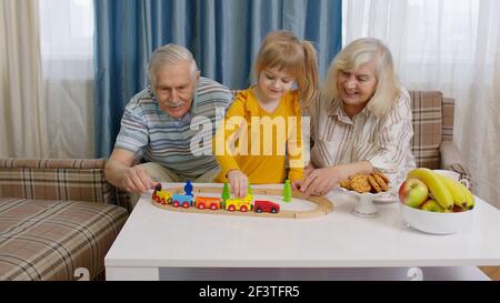 Mature couple grandmother, grandfather with child girl grandkid riding toy train on railroad at home Stock Photo