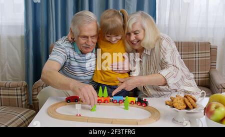 Senior grandparents with child kid granddaughter playing game, riding toy train on railway at home Stock Photo