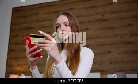 Woman hold in hands credit bank card using mobile cell phone order delivery, online shopping payment Stock Photo