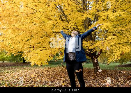 A woman stands by a tree and enjoys the leaves falling in autumn at the Finch Arboretum in Spokane, Washington USA. Stock Photo