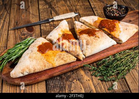 Cut and sliced Calzone closed pizza with ham and cheese on wooden board with hot tomato sauce. wooden background. Top view Stock Photo