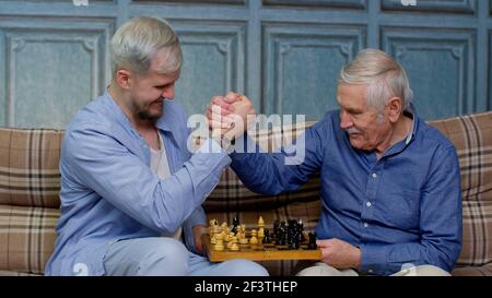 Happy different male generations family of senior father and adult son or grandson playing chess Stock Photo