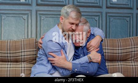 Adult man son hugging and consoling sadness old age father with love, mental health, social problems Stock Photo
