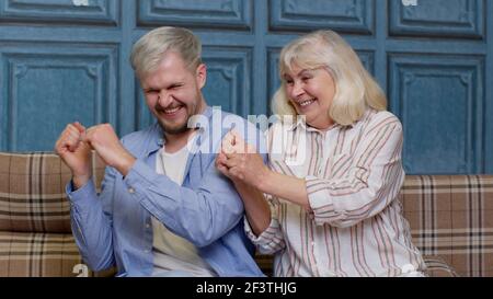 Generations family of senior mother and handsome adult son or grandson dancing together, laughing Stock Photo