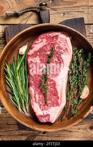 Fresh new york strip beef meat steak or striploin in a wooden plate with herbs. wooden background. Top view Stock Photo