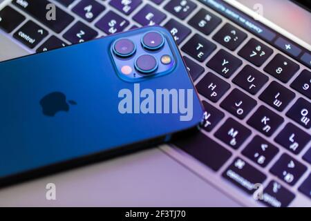 Chernivtsi, Ukraine - march, 2021: Apple iphone 12 Pro Max blue smartphone over macbook laptop on wooden table in the office Stock Photo