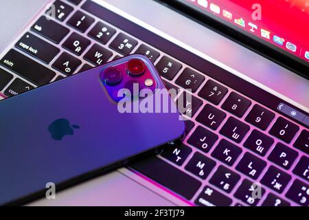 Chernivtsi, Ukraine - march, 2021: Apple iphone 12 Pro Max blue smartphone over macbook laptop on wooden table in the office Stock Photo