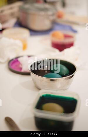 Colourful eggs in dye in plastic and metal bowls on a messy kitchen surface, family traditions for Easter Stock Photo