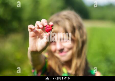 Blurred girl shows blurry strawberries on a blurred green nature background. Field, forest. Harmony with nature. Out of focus Stock Photo