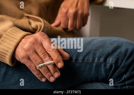 Detail shot of the hand of an elderly Caucasian man with wrinkled hands sitting smoking a cigarette. Stock Photo