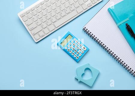 Calculator with model of house, stationery and computer keyboard on color background Stock Photo
