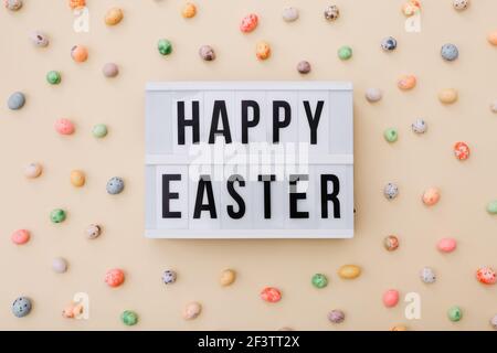 Easter wishes on lightbox with chocolate mini eggs scattered on a beige background, top view Stock Photo