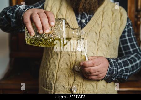 Close up on hands of unknown man pouring traditional serbian bosnian croatian or macedonian drink alcohol brandy rakija or slivovitza made from plum i Stock Photo