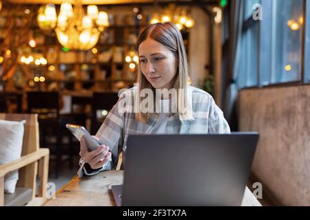 Young Caucasian business woman with blonde hair working on laptop in cafe. College student using technology , online education, freelance  Stock Photo