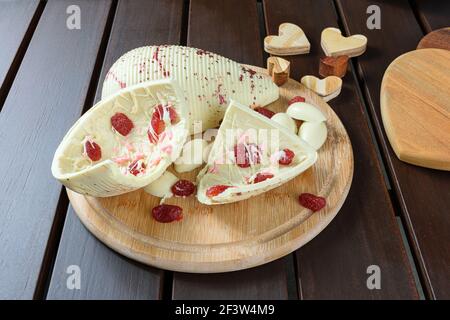 Half a broken Easter egg. White chocolate with candied strawberries on a wooden plate next to hearts. Stock Photo