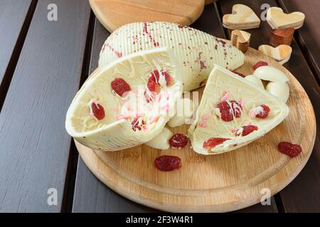 Closeup of half a broken Easter egg. White chocolate with candied strawberries on a wooden board next to hearts. Stock Photo