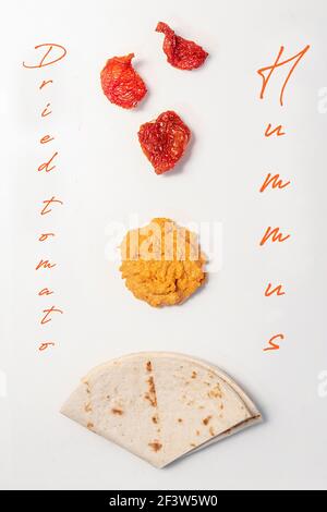 Top view of three pieces of dried tomato, hummus and pita bread on white background Stock Photo