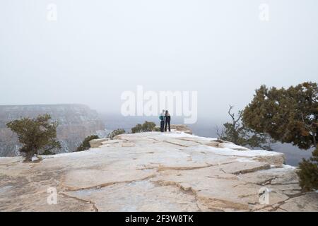 Couple stand romantically on rim of Grand Canyon during winter snow Stock Photo