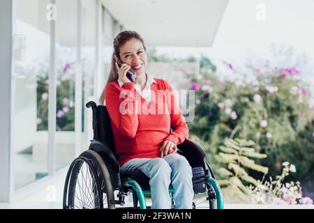 Young latin woman talking by phone in wheelchair at workplace in Mexico city Stock Photo