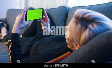 Caucasian woman relaxing on the couch and holding smartphone with green screen. High quality photo Stock Photo
