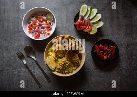 Popular mughlai cuisine biryani in a bowl along with salad condiments Stock Photo