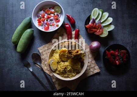 Top view of  Popular mughlai cuisine biryani in a bowl along with salad condiments Stock Photo