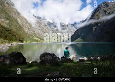 A tourist eating an apple and enjoying the views of Lake Marian - an alpine lake in a beautiful hanging valley, Fiordland National Park, New Zealand Stock Photo