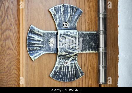 Forged aged patinated cross-shaped ornamented door hinge on wooden vintage church door. Stock Photo
