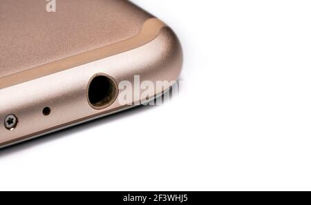 Closeup detail of 3.5mm audio jack connector hole on bottom of rose gold coloured mobile phone, isolated white background Stock Photo