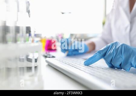 Scientist hands in gloves working on the keyboard at desktop Stock Photo