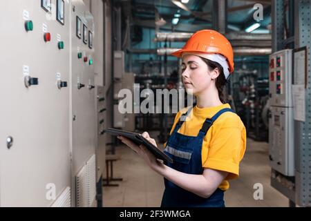 Concept of industrial production and equality. Portrait of a female engineer in uniform and helmet with a tablet in her hand. In the background-boiler Stock Photo