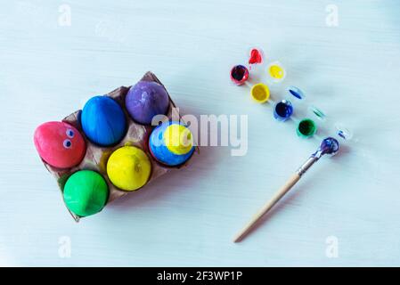 Painted eggs, paints and a paintbrush on a white table. Easter concept. Top view, flat lay. Stock Photo