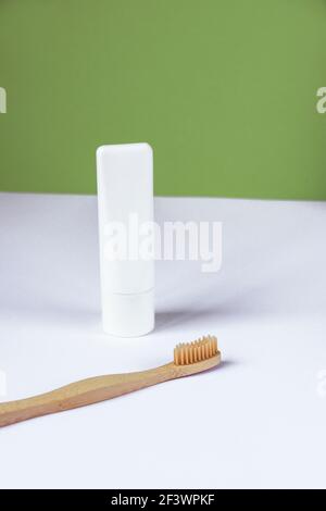 White tube of toothpaste and toothbrush on white table against green wall background. Personal hygiene and self-care concept. Front view. Stock Photo