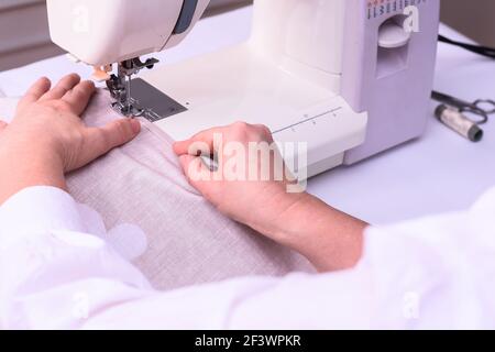 Female hands stitching white fabric on machine. Seamstress hands holding textile for linen.  Stock Photo