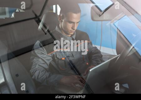 Repairman examining car with laptop, working diagnostic on damaged car Stock Photo