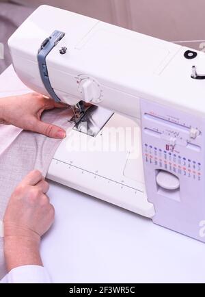 Female hands stitching light fabric on machine. Stock Photo