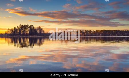 Epic red sunset sky above the lake and forest. Dramatic cloudscape. Symmetry reflections on the water, natural mirror Stock Photo
