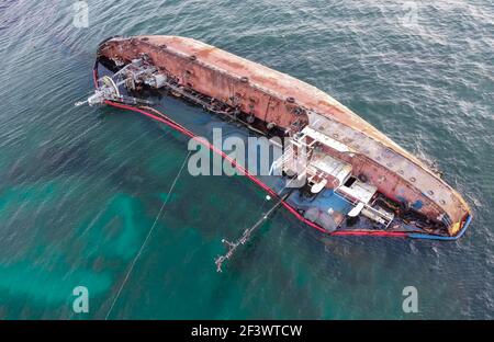 The ship ran aground and capsized, spilling oil into the sea. Ecological catastrophe on the coast. Stock Photo