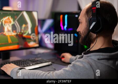 Digital player wearing headphones playing videogame with modern graphics for shooter game championship. Online streaming cyber performing during gaming tournament using powerful PC with RGB Stock Photo