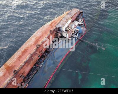 An old rusty tanker lies on the beach sideways. The storm-swept vessel pollutes the water with oil Stock Photo