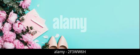 Feminine workspace with notebook, shoes, pink peony, eucalyptus flower on blue background. Top view, copy space. Blogger, feminine business concept Stock Photo