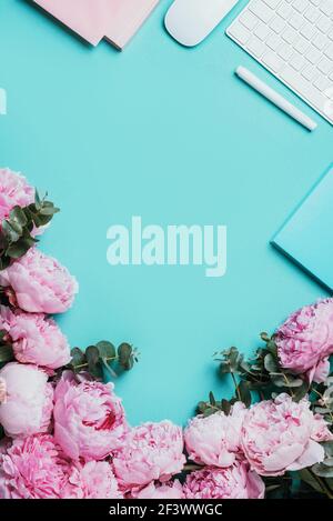 White computer keyboard, mouse, peony flowers, eucalyptus flowers on blue background. Top view. Copy space. Flat lay. Feminine workspace. Blogger Stock Photo